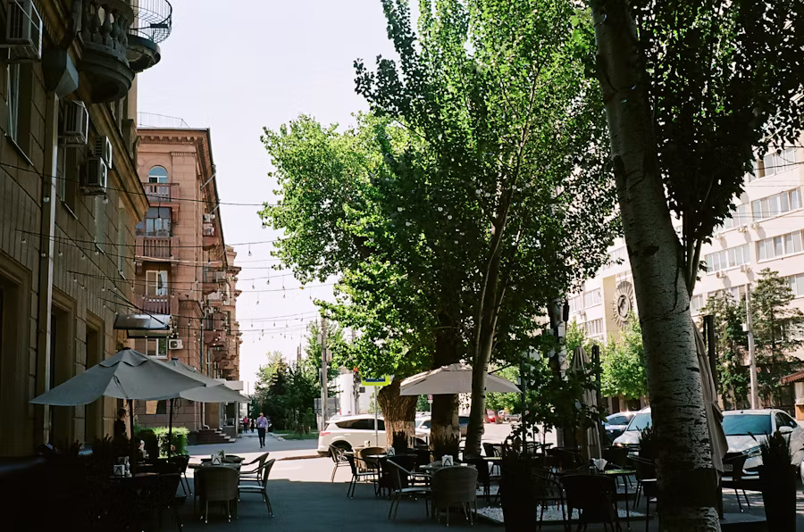 Walkable downtown street with sidewalk cafés, mature trees, and urban energy — the Royal Oak feeling